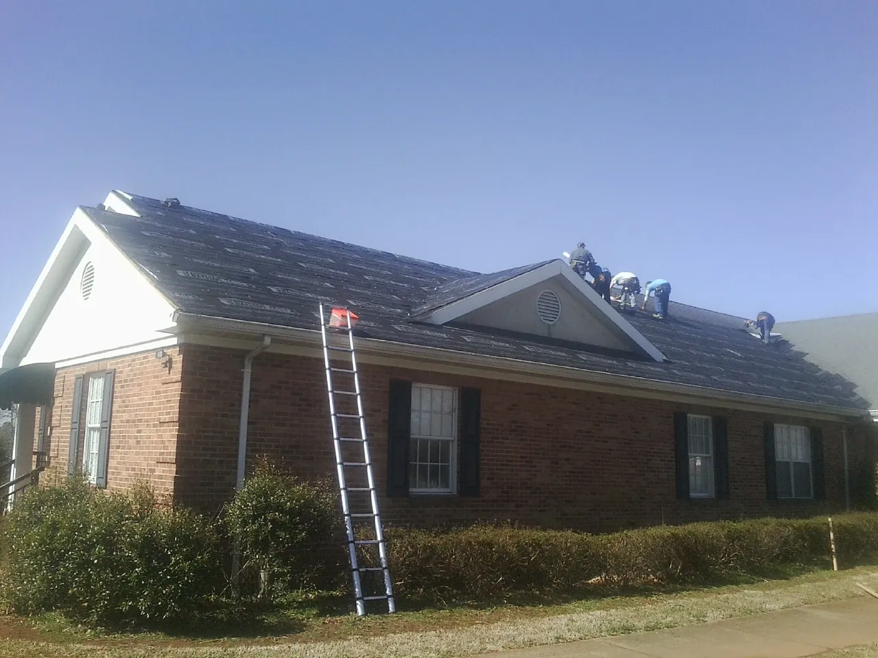 Crew tearing shingles off a brick ranch roof with a ladder set — Metal Roof Repair work by our crew in Joseph