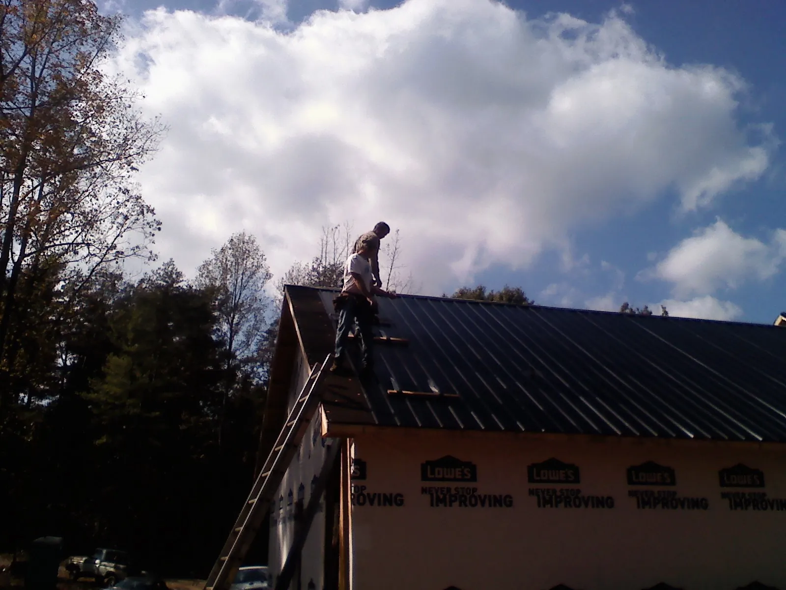 Roofer fastening dark metal panels high against a cloudy sky, from a Roof Inspection job in Joseph