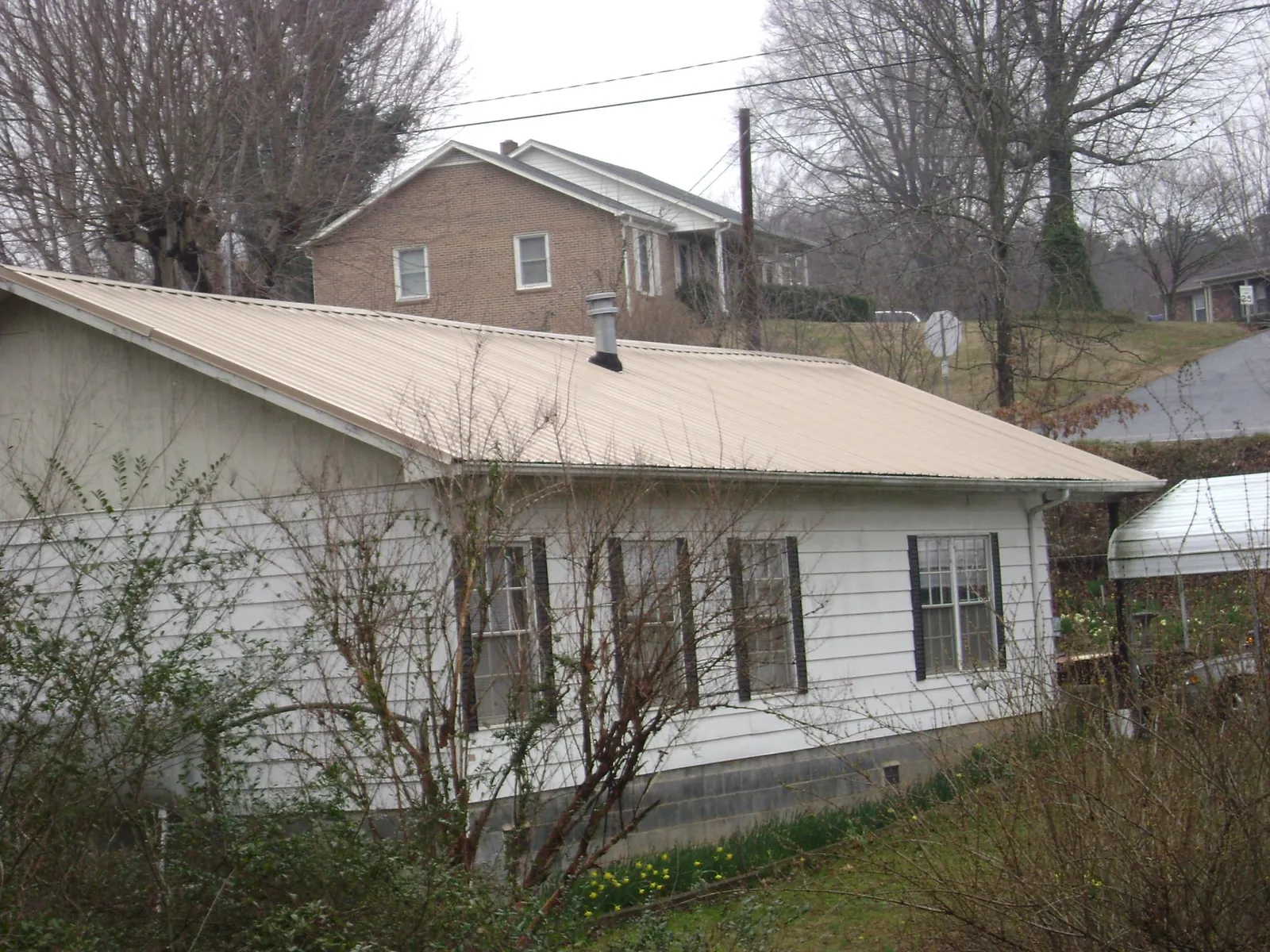 Tan metal roof on a white sided house set into a hillside — Commercial Roofing by Roofing Brothers in Joseph